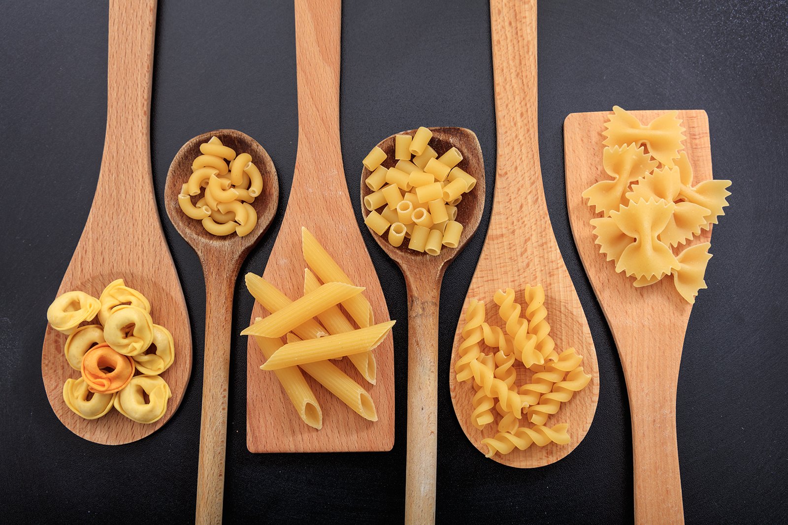 Different types of pasta shapes sitting on wooden spatulas