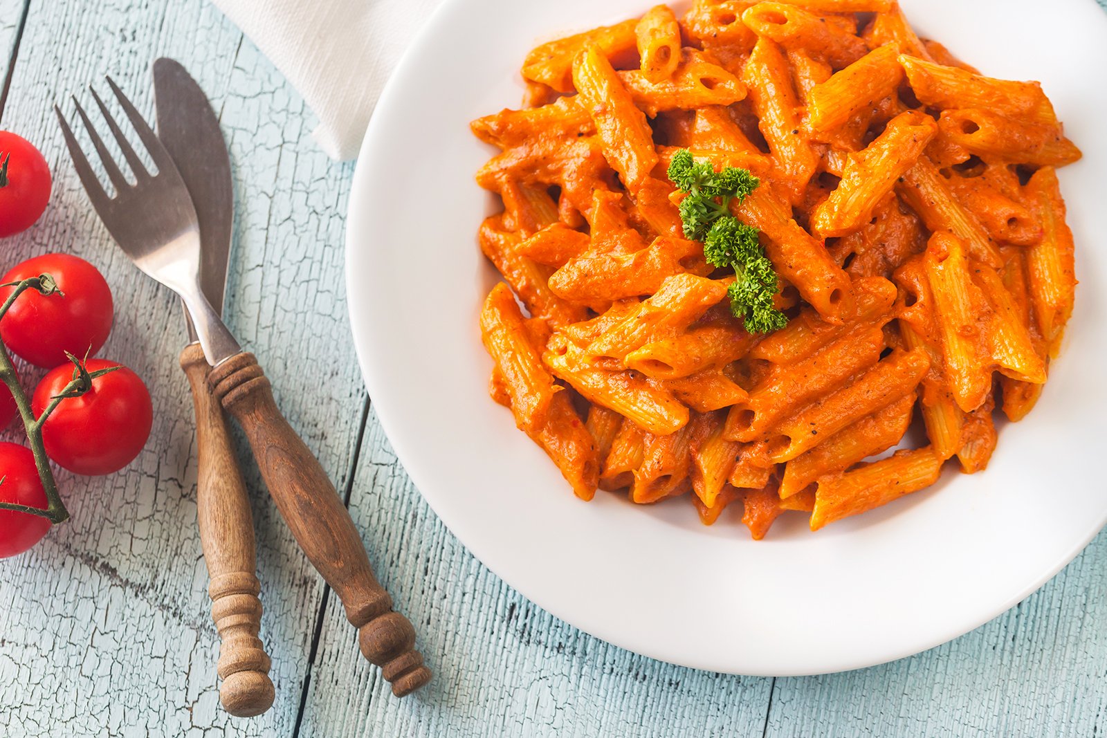 Penne ala vodka on plate with utensils and tomatoes on the side