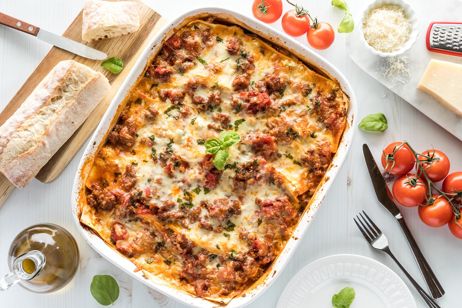 Overhead shot of lasagna dish with olive oil, tomatoes and bread