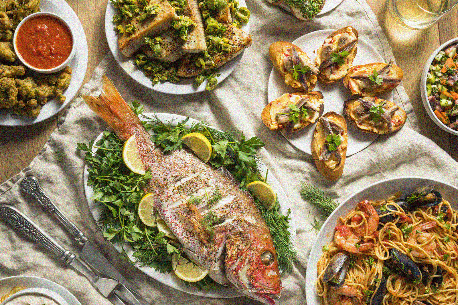 assortment of dishes on a table including fish, spaghetti with seafood, bread