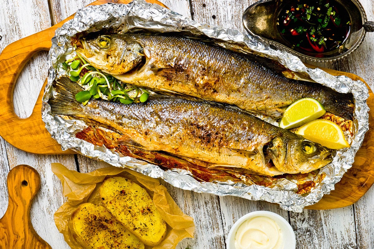 roasted branzino on a wood cutting board with lemons on the side