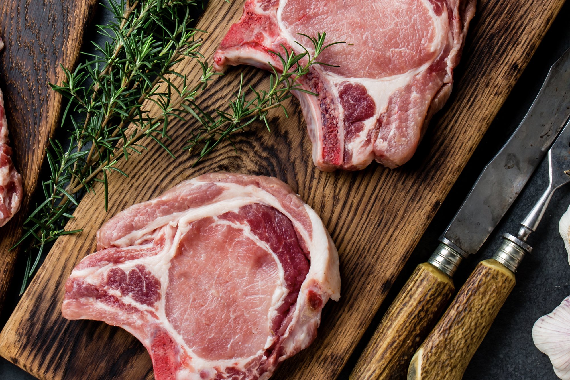 Raw pork chops on cutting board with herbs around