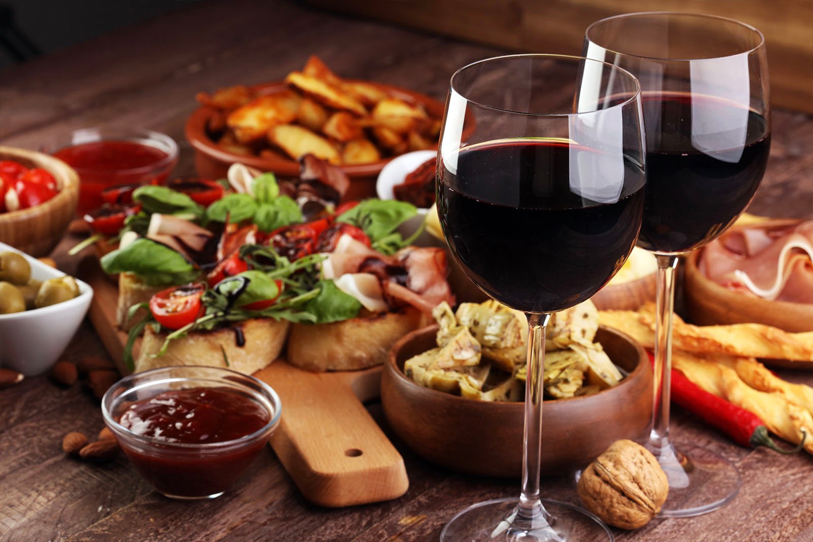 Italian antipasti wine snacks set: cheese variety, Mediterranean olives, pickles, Prosciutto di Parma, tomatoes, artichokes and wine in glasses